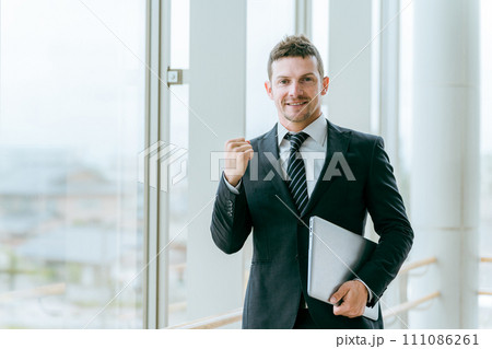 ノートパソコンを持ってガッツポーズをする外国人ビジネスマン（白人男性・応援・成功・やる気） 111086261