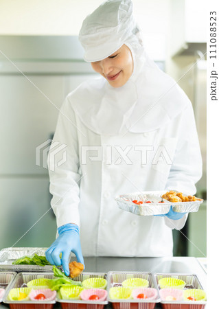 クリーンスーツでお惣菜を詰める若い女性 クリーンスーツでお惣菜を詰める若い女性 111088523