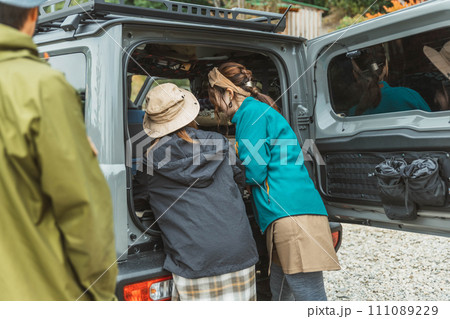 秋冬のアウトドア・キャンプ場にキャンプに来て車の荷台から荷物を運ぶ仲間達（アジア人） 111089229