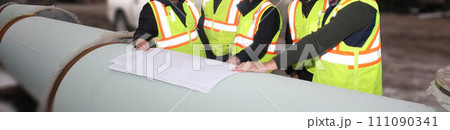 Several construction engineers, dressed in construction vests, are examining plans at the job site. 111090341