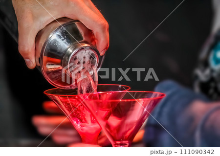 A close up to bartender expertly pouring a mixed drink, gracefully pouring it into a martini glass. 111090342