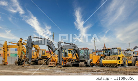 Various heavy construction vehicles, such as excavators, diggers, earthmovers, and bulldozers, are stationed at a construction site throughout the winter season. 111090350