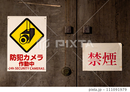 扉に防犯カメラと禁煙のシールが貼られている風景 111091979