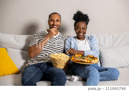 Man and woman family enjoying movie on weekend eating pizza and popcorn while sitting on couch 111093798