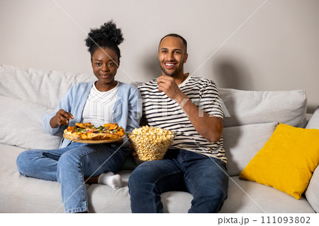Couple eating pizza and popcorn watching comedy film sitting on couch indoor 111093802