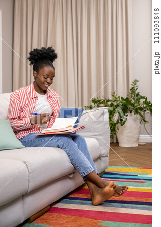 Woman writing to do list or plan for day while sitting on couch in home interior. 111093848