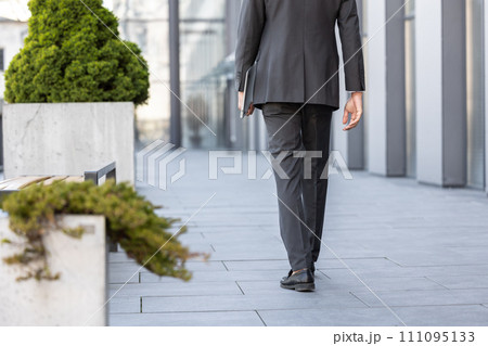 Close up of elegant man with a laptop in hands walking 111095133