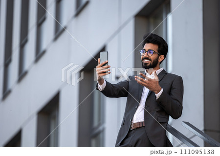 Brunette hindu young man on the building background with phone in hand Brunette hindu young man on the building background with phone in hand 111095138