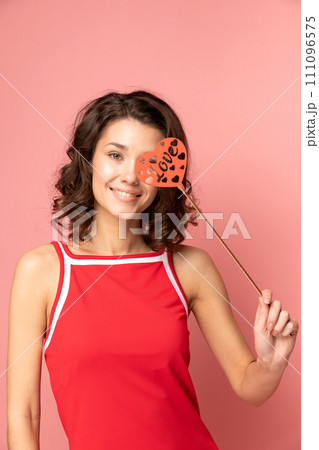 Portrait of young lady stands on pink background with heart shapped decoration 111096575