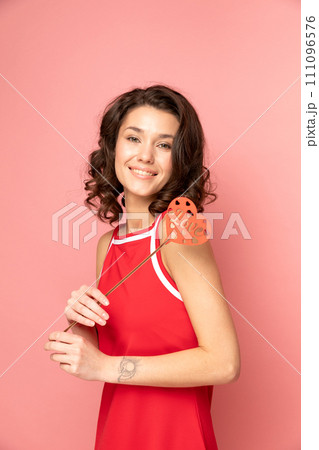 Portrait of young lady stands on pink background with heart shapped decoration 111096576