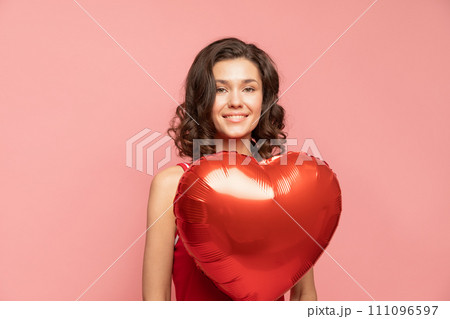 Portrait of young lady stands on pink background with heart shapped decoration Portrait of young lady stands on pink background with heart shapped decoration 111096597