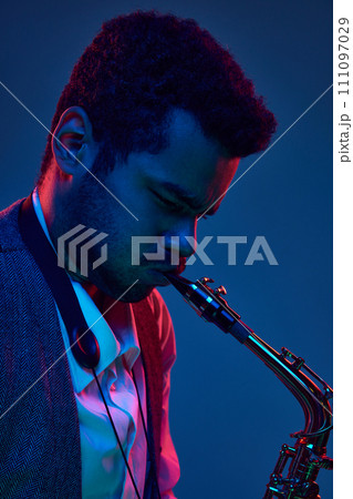 Music therapy. African-American man playing on saxophone, jazz and blues melodies against gradient blue background in neon light. 111097029