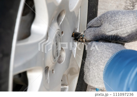 Hand holds the pressure gauge and fills the car tires with air. Car maintenance. 111097236