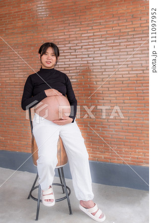 Mom pregnant woman in a dress holds hands on belly on red brick background, Waiting for the birth of your baby with love 111097952