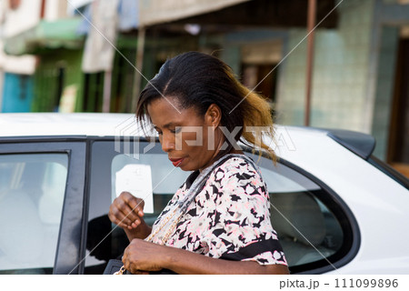 Young happy smiling woman standing in front of a new luxury car and look in his handbag. Young happy smiling woman standing in front of a new luxury car and look in his handbag. 111099896