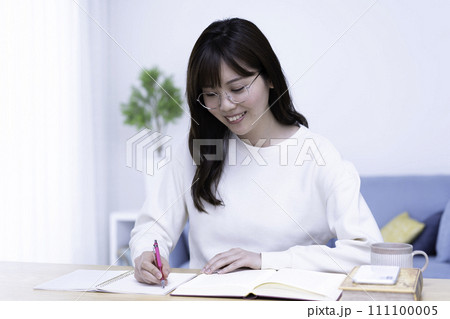 明るいリビングで勉強する眼鏡の女性 111100005