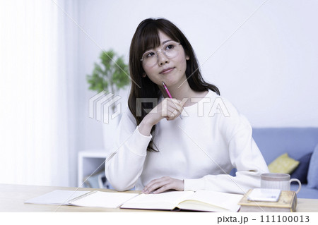 明るいリビングで勉強する眼鏡の女性 111100013