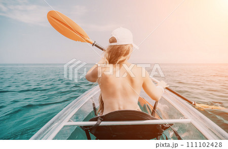 Woman in kayak back view. Happy young woman with long hair floating in transparent kayak on the crystal clear sea. Summer holiday vacation and cheerful female people relaxing having fun on the boat 111102428