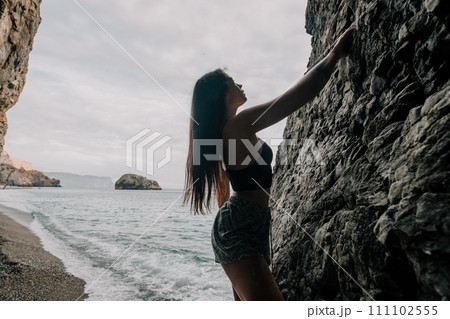 Sports Woman Climbing The Rock. Young woman With slim fit body climbing in volcanic basalt cave with beautiful sea view. The athlete girl trains in nature. Woman overcomes difficult climbing route. Sports Woman Climbing The Rock. Young woman With slim fit body climbing in volcanic basalt cave with beautiful sea view. The athlete girl trains in nature. Woman overcomes difficult climbing route. 111102555