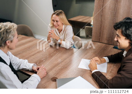 High-angle view of happy male CEO boss manager telling funny joke, having fun talking with employees during group briefing. Cheerful friendly business team laughing sitting at meeting table 111112724