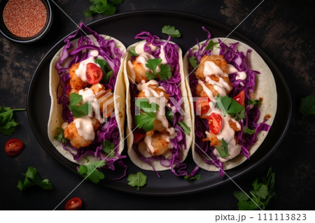 Top view of Bang Bang shrimp Tacos with purple coleslaw, tomato and sauce on the black plate 111113823