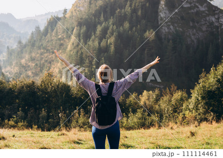 Woman hiker with backpack open arms at mountain peak. Travel and active lifestyle concept. 30s girl enjoying valley view from top of a mountain, outdoor activities, back view 111114461
