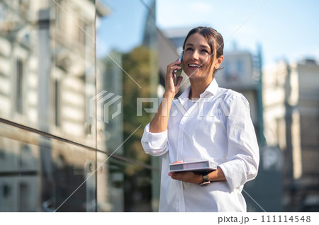 Pretty businessman with the phone and notebook in hands in the street 111114548