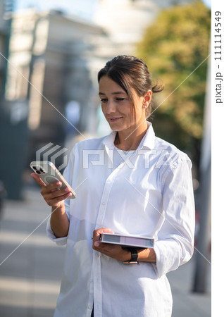 Pretty businessman with the phone and notebook in hands in the street 111114549