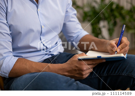 Man sitting on sofa at home and writing notes in notebook Man sitting on sofa at home and writing notes in notebook 111114589