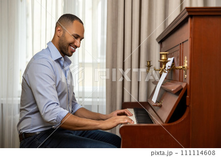 Man practicing playing piano in living room of his home relaxing from work 111114608