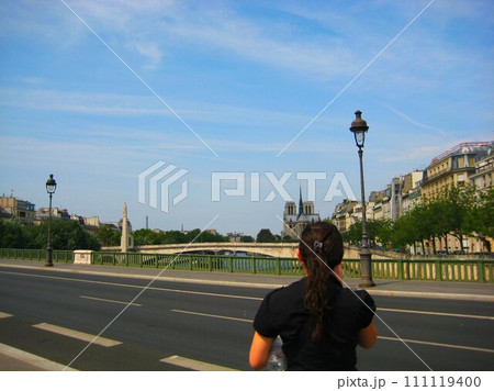 フランス、パリのセーヌ川の橋でノートルダム大聖堂を見る女性 フランス、パリのセーヌ川の橋でノートルダム大聖堂を見る女性 111119400