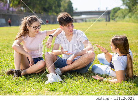 Cheerful teen boy and girls talking on green lawn Cheerful teen boy and girls talking on green lawn 111120025