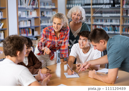 Group of schoolchildren with a female teacher in the library, discussing something 111120489