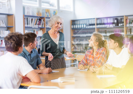 Group of schoolchildren with a female teacher in the library, discussing something Group of schoolchildren with a female teacher in the library, discussing something 111120559