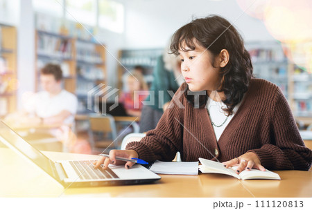 Schoolgirl studies on a laptop and writes notes in a copybook Schoolgirl studies on a laptop and writes notes in a copybook 111120813