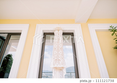 White wedding dress with a train hanging on a hanger on the balcony 111121738