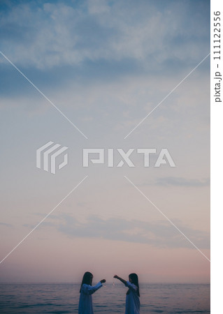 夕日バックに花火をする若い女性のシルエット 夕日バックに花火をする若い女性のシルエット 111122556