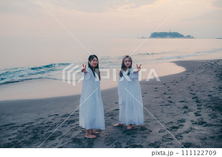 夕焼けバックに記念写真を撮る若い女性 111122709