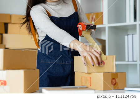Young business entrepreneur sealing a box with tape. Preparing for shipping, Packing, online selling, e-commerce concept Young business entrepreneur sealing a box with tape. Preparing for shipping, Packing, online selling, e-commerce concept 111124759
