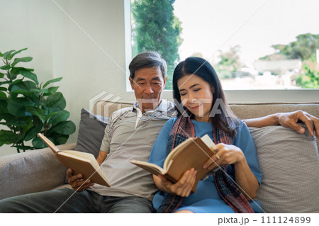 Retired elderly couple sits on couch in their home reading relaxing book. Senior Activity Concept 111124899
