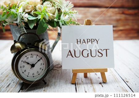 Happy August text message written on paper card with wooden easel and alarm clock with flower in metal vase decoration Happy August text message written on paper card with wooden easel and alarm clock with flower in metal vase decoration 111126514