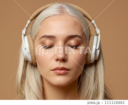 Close-up portrait of a young blonde woman wearing beige headphones. 111128862
