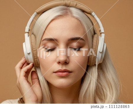 Close-up portrait of a young blonde woman wearing beige headphones. 111128863