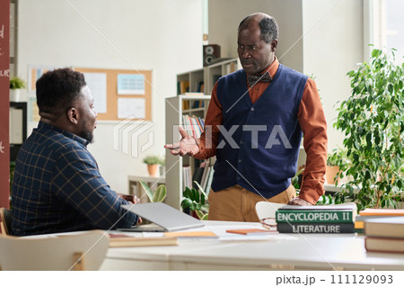 Portrait of Black senior professor consulting student during one on one meeting in school classroom 111129093