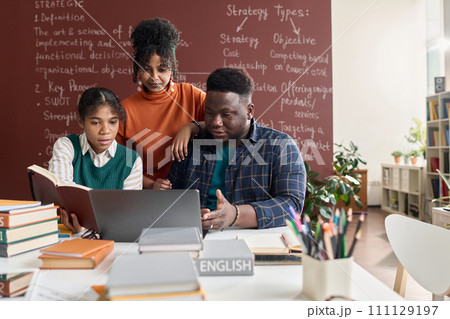 Front view portrait of three Black young people using laptop together while working on group project in school 111129197