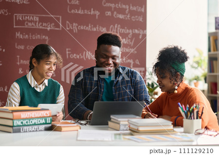 Group of three Black young people smiling happily while doing schoolwork together in college class and looking at laptop screen 111129210