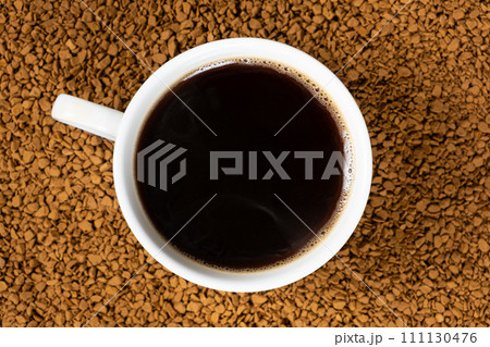 A cup of hot instant coffee on a background of freeze-dried granules 111130476