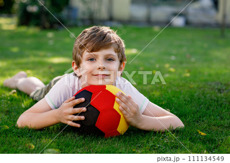 Happy active kid boy playing soccer with ball in German flag colors. Healthy child having fun with football game and action outdoors Happy active kid boy playing soccer with ball in German flag colors. Healthy child having fun with football game and action outdoors 111134549