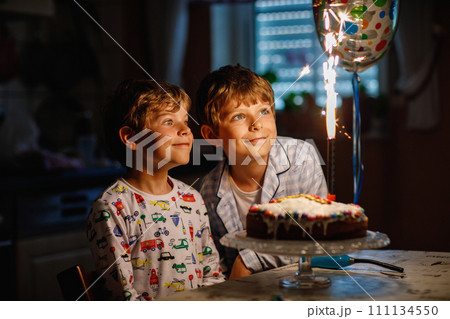 Two beautiful kids, little preschool boys celebrating birthday and blowing candles on homemade baked cake, indoor. Birthday party for siblings children. Happy twins about gifts and fireworks on tarte Two beautiful kids, little preschool boys celebrating birthday and blowing candles on homemade baked cake, indoor. Birthday party for siblings children. Happy twins about gifts and fireworks on tarte 111134550