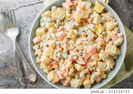 Delicious potato salad with green peas, carrots, corn and apple covered with mayonnaise close-up on a plate. Horizontal top view Delicious potato salad with green peas, carrots, corn and apple covered with mayonnaise close-up on a plate. Horizontal top view 111134735